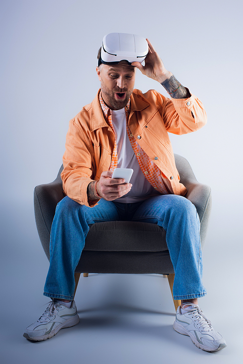 A man sits in a chair staring at a cell phone, deep in thought.