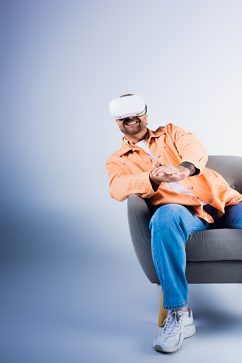 A happy man wearing a VR headset sits in a chair in a studio setting.