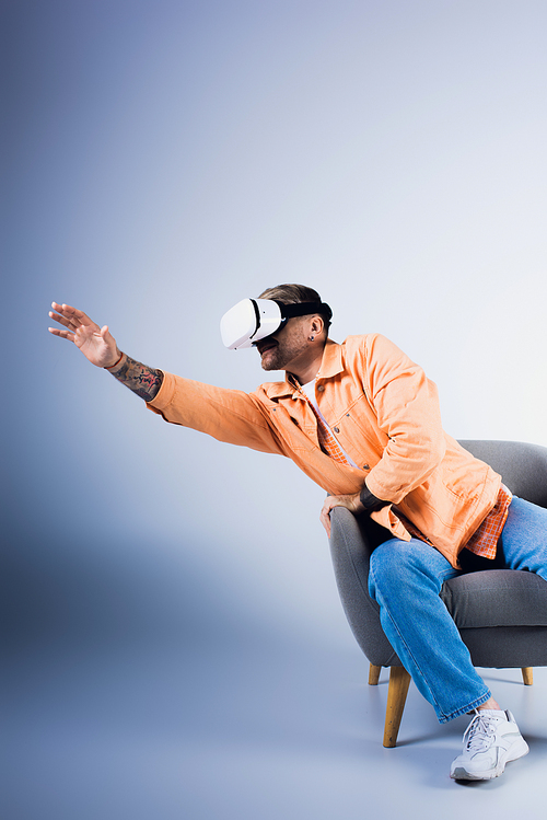 A man in a VR headset sits in a chair with his hand raised, immersed in a virtual world