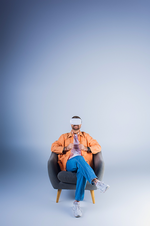 A man in a VR headset comfortably lounging in a chair with his feet up in a studio setting.