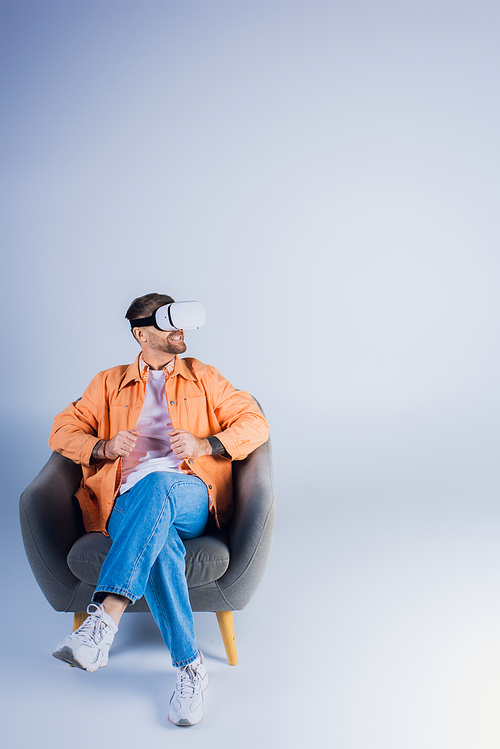 A man in a VR headset comfortably lounging in a chair in a studio setting.