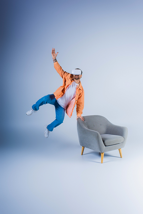 A person wearing a VR headset jumps energetically next to a chair in a studio setting.