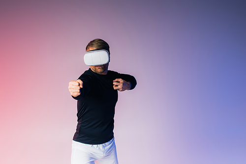 A man, blindfolded, stands before a vibrant pink and blue background in a surreal studio setting.