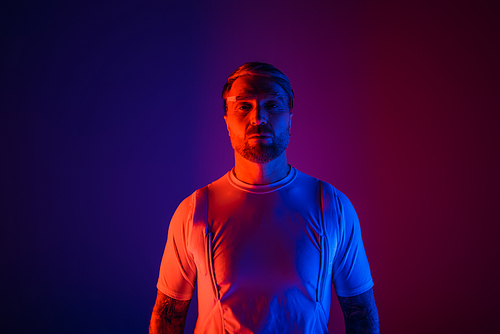 A man in smart glasses stands confidently in front of a vibrant purple and blue background in a futuristic studio setting.