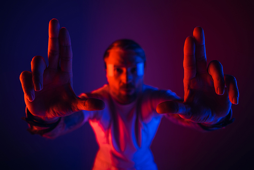 A man in a white shirt stands in a studio setting wearing smart glasses and holding up two fingers.