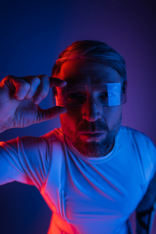 A man in smart glasses stands confidently in front of a vibrant red and blue background in a studio setting.