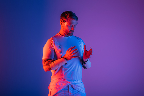 A man in smart glasses stands confidently in a studio setting against a vibrant purple and blue background, evoking a sense of virtual reality.