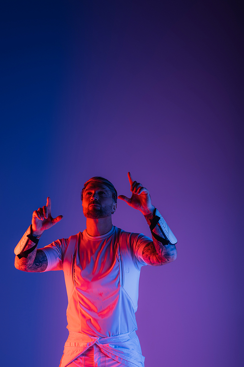 A man with smart glasses stands confidently against a vibrant purple and blue backdrop in a studio setting.