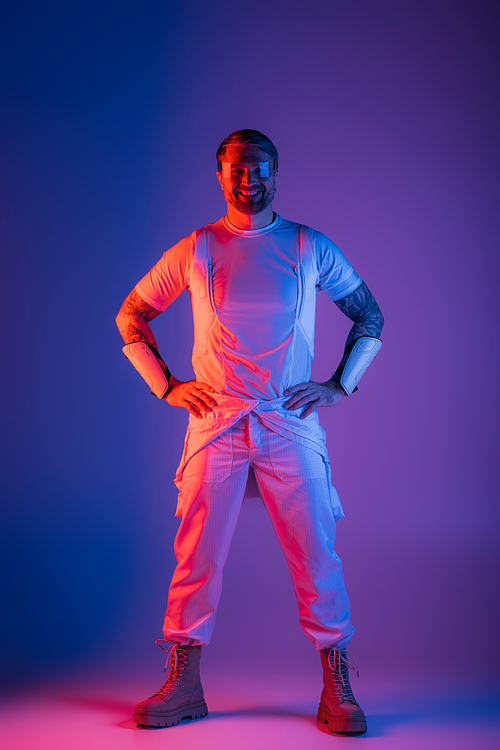 A man wearing smart glasses stands confidently in front of a vibrant purple and blue background, embodying the digital world of the metaverse.