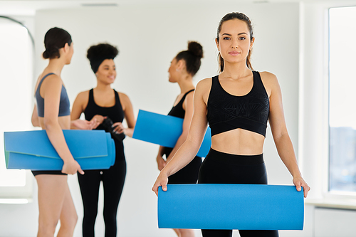 focus on brunette young woman in sportswear standing with fitness mat next to interracial friends