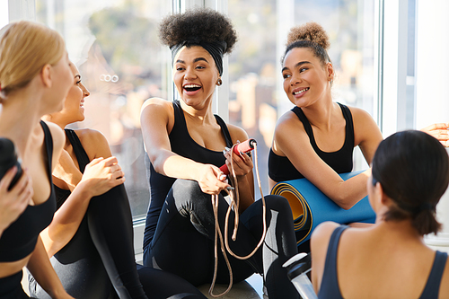 group of happy young interracial women in active wear chatting after workout in pilates studio