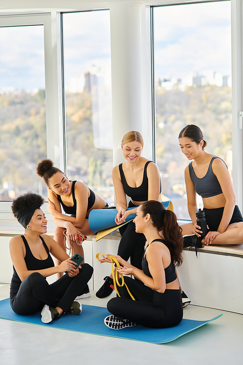 group of young five interracial woman in sportswear chatting after workout in pilates class, friends