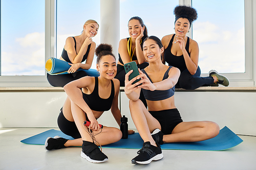 group of five and cheerful interracial female friends in sportswear taking selfie after yoga class