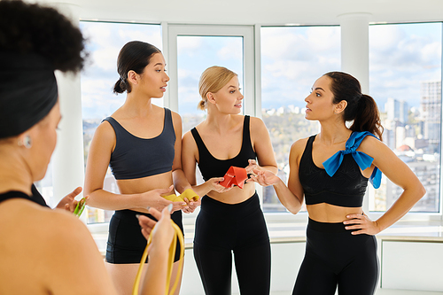 group of motivated and serious sportswomen holding resistance bands and chatting after pilates class