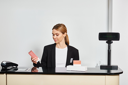 good looking shop assistant in sophisticated black blazer sitting at counter and looking at perfumes