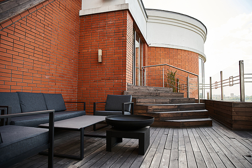 A serene wooden deck adorned with stylish black furniture sits against a backdrop of a charming brick building