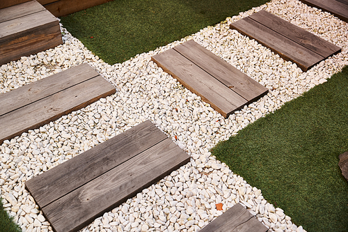 A serene garden space featuring wooden steps leading down to a gravel pathway surrounded by lush greenery and decorative elements