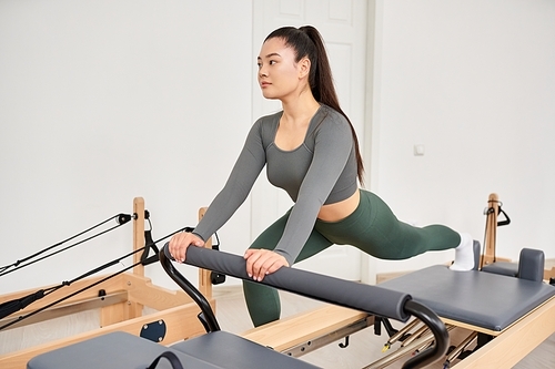 A sporty woman in gray shirt, green pants on Pilates lesson.