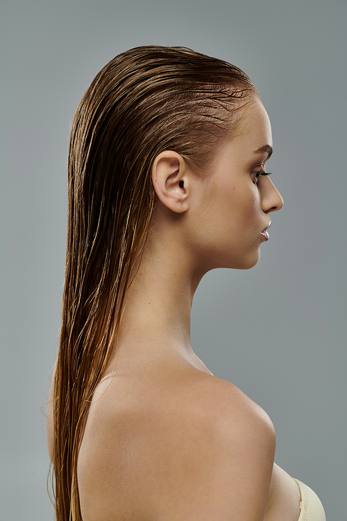 Young woman posing with wet hair on gray backdrop.