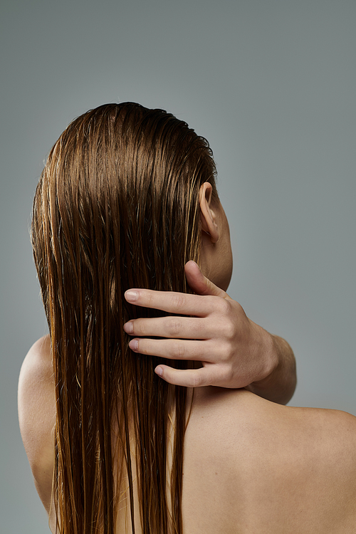 Appealing woman with long hair is gently touching her wet hair.