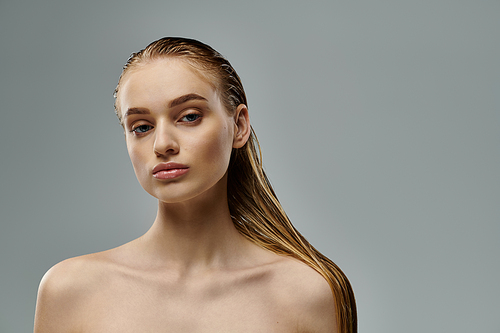 Young woman showcasing her wet hair on a gray backdrop.