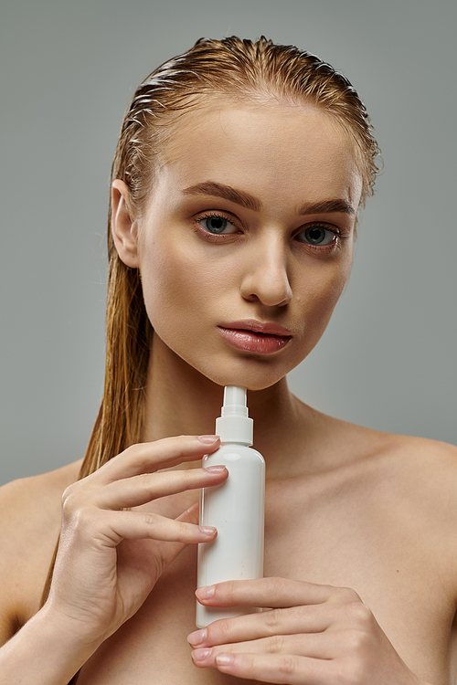 A young, beautiful woman holding a bottle of lotion, tending to her hair.