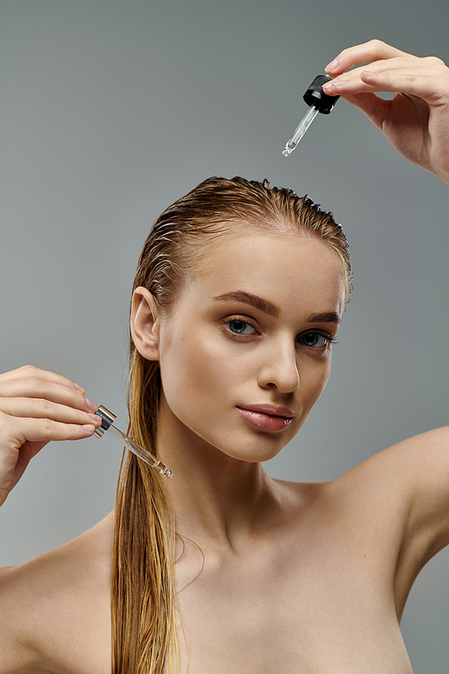 Young woman using hair oil on gray backdrop.