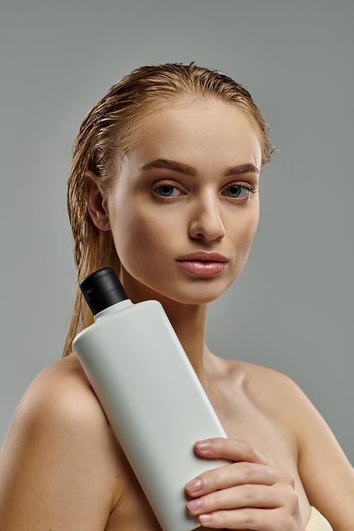 A young woman showcases her hair care routine holding a bottle of shampoo.