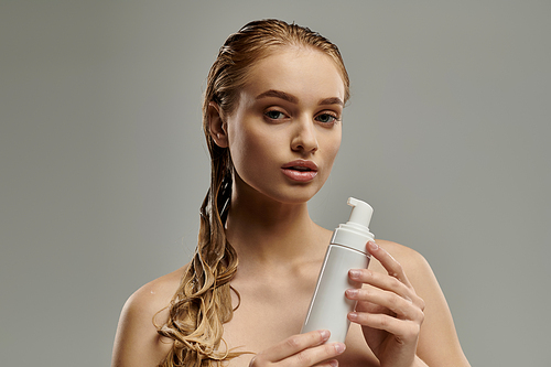 A young woman with wet hair holds a bottle of lotion in her hands, showcasing her hair care routine.