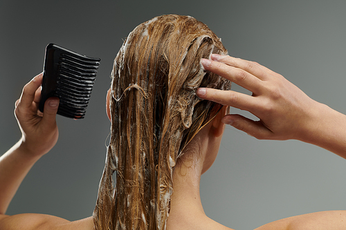 A young woman is brushing her hair with a comb after a hair wash.