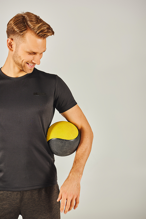 Young sportsman in black t-shirt holding a yellow ball in a studio with a grey background.