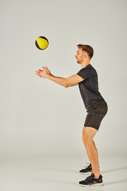 A young sportsman in active wear catches a yellow and black ball in a dynamic studio setting with a grey background.