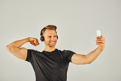 A young sportsman in active wear taking a selfie with his phone in a studio with a grey background.