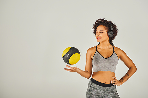 Curly African American sportswoman in active wear showcases strength and balance as she holds a vibrant yellow and black ball.