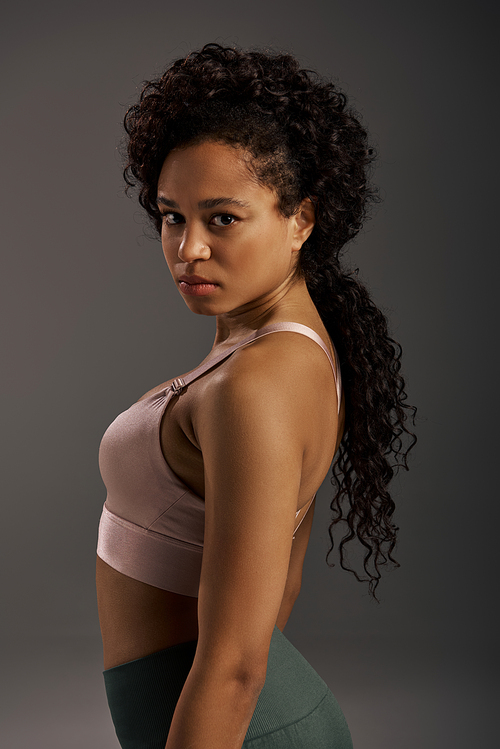 Curly African American sportswoman in active wear working out in a studio with a grey background.