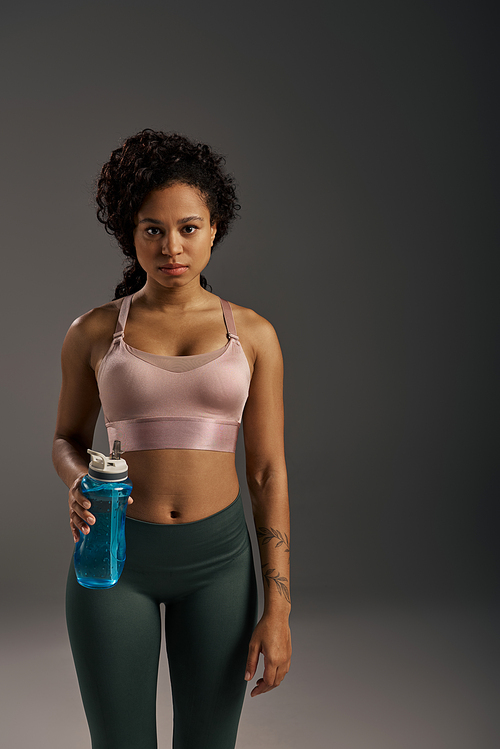 A curly African American sportswoman in tank top and leggings hydrating with a water bottle during workout session.