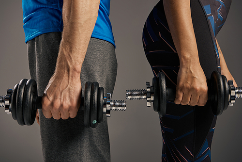 Fit multicultural couple in activewear holding dumbbells as they exercise in a studio against a grey backdrop.