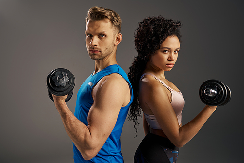 A fit and multicultural young couple poses confidently with dumbbells in an active wear studio setting.