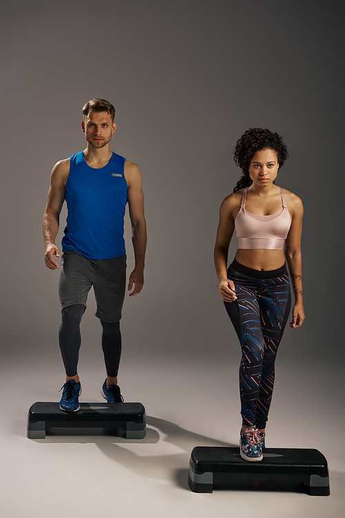 Multicultural, fit couple in active wear balancing on steppers in studio workout session.