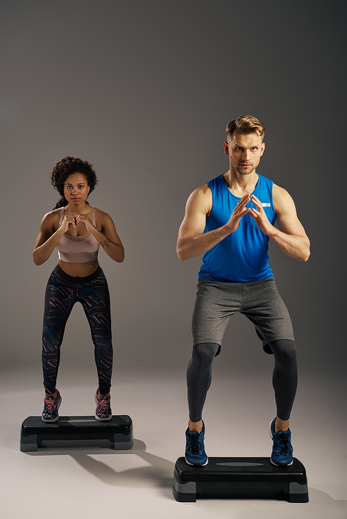 Multicultural, fit couple in active wear working out on steppers in a studio setting.