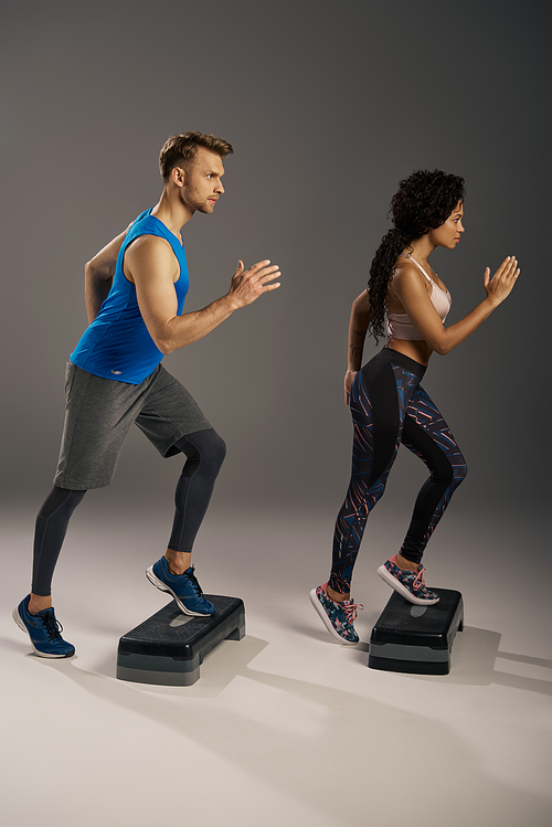 A young multicultural couple in active wear running energetically on steppers in a studio setting.