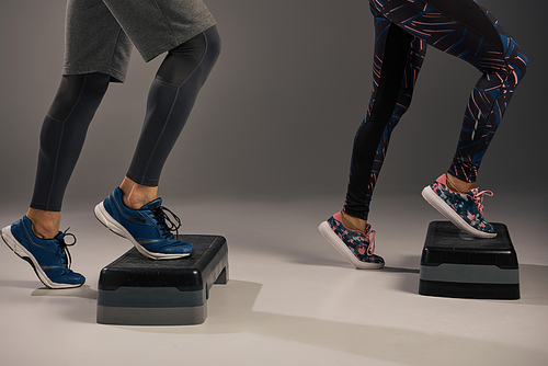 A young multicultural and fit couple wearing active attire balancing on a pair of steppers in a studio setting.