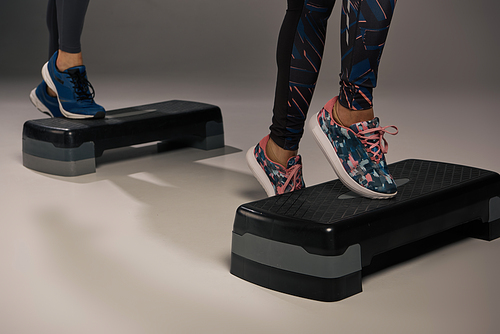 A young multicultural and fit couple in active wear, energetically standing on a pair of steppers in a studio setting.