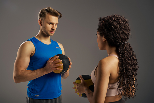 A multicultural couple in active wear grips a weighted ball, showcasing strength and determination in a studio setting.