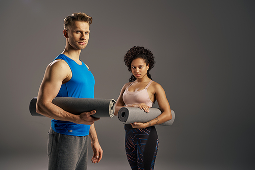 A young multicultural and fit couple in active wear holding a yoga mat, ready for their workout in a studio setting.