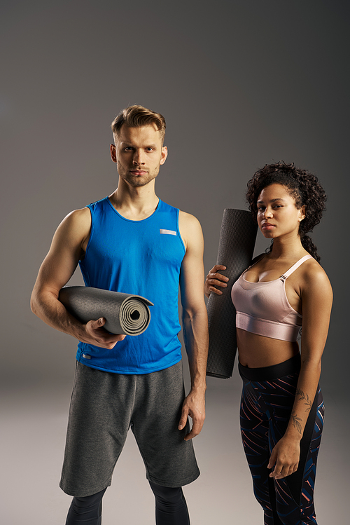 Young multicultural couple in active wear posing with yoga mat in a studio setting.