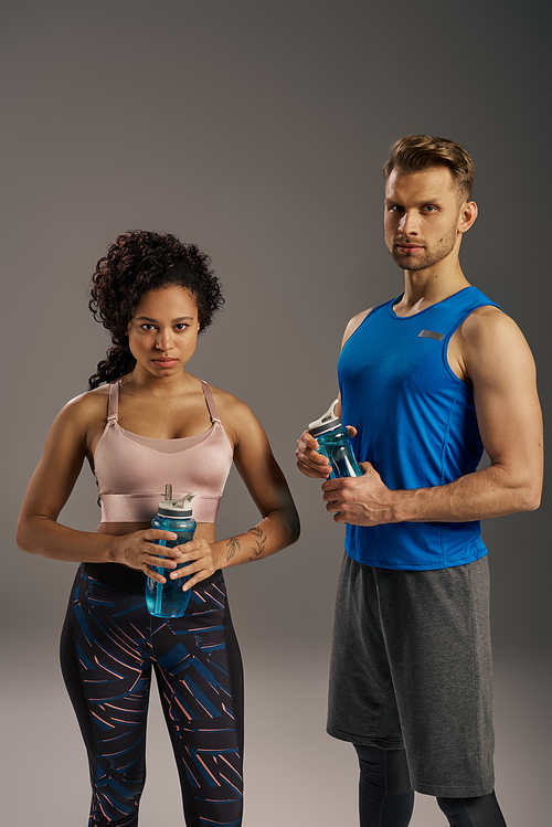 A young multicultural couple in active wear posing gracefully for a portrait on a grey studio background.