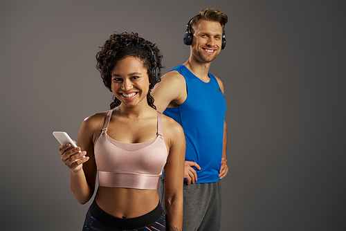 A young, multicultural couple stands together, holding a cell phone, sharing a moment of connection on a grey background.