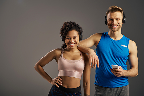 A young, multicultural couple in active wear pose and groove to music in a studio setting.