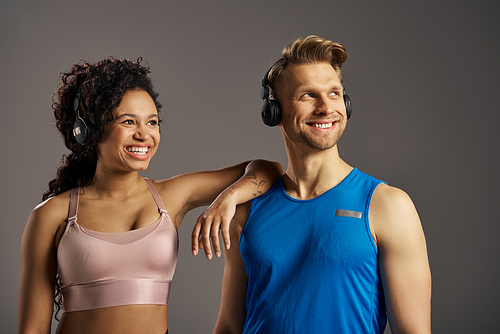 A young multicultural and fit couple, dressed in active wear, are striking a pose for a photo while wearing headphones.